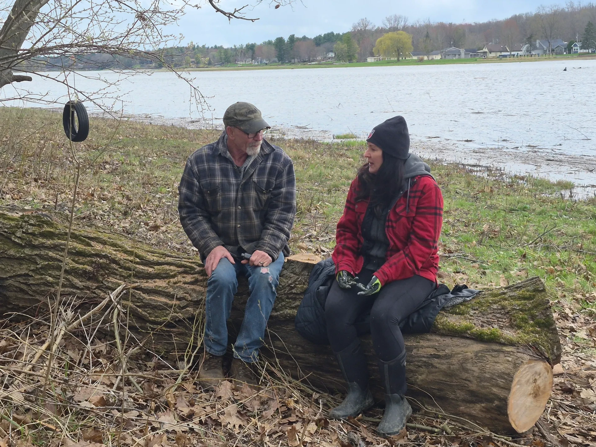 A veteran and a companion sitting on a fallen log and talking beside a lake